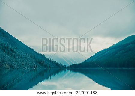 Amazing Silhouettes Of Mountains And Low Clouds Reflected On Mountain Lake. Beautiful Ripples On Wat
