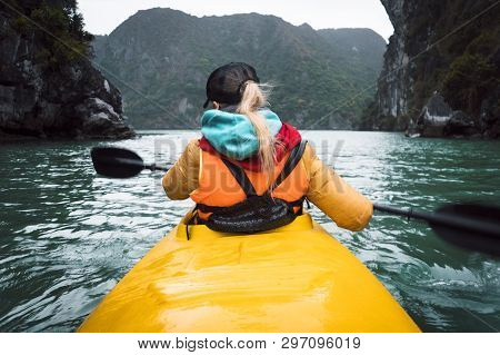 Young Beautiful Woman Floating On A Kayak Between The Rocks Sticking Out Of The Sea. The Girl Rowing