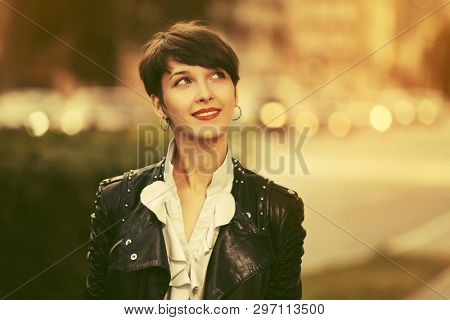 Happy young fashion woman with pixie hair walking on city street Stylish female model wearing black leather jacket and white blouse
