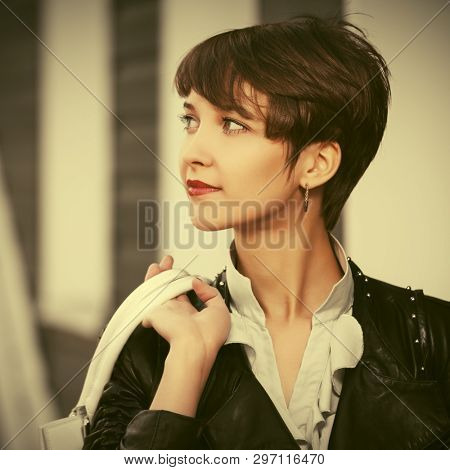 Happy young fashion woman walking on city street Stylish female model in black leather jacket with pixie haircut