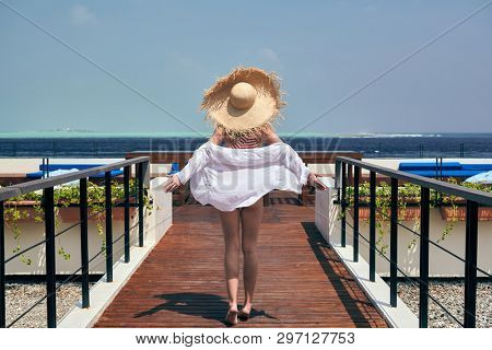 Woman in red striped one-piece swimsuit walking on tropical beach patio deck. Summer vacation at Maldives.