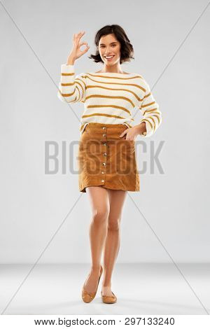 people concept - happy smiling young woman in striped pullover, short skirt and ballet flat shoes showing ok gesture over grey background