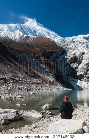 Young Woman Watching Beautiful View Of Manaslu Mountain Range, Birendra Lake.  Lady Sits In Front Of