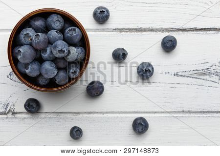 Blueberries Spilling Out Of A Bowl On Distressed White Wooden Background