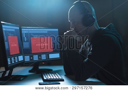 cybercrime, hacking, wiretapping and technology concept - male hacker in headphones with access denied message on computer screen using virus program for cyber attack in dark room