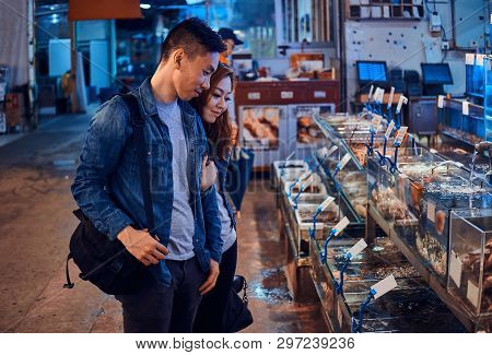 Romantic Asian Couple Looking For Something Special At Seafood Chainese Market. They Are Curious And