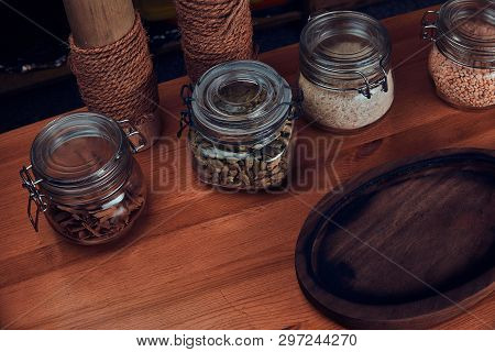 There Are Empty Round Wooden Tray, Cordamom, Cinnamon Bark, Nuts And Pepercorns In Glass Jars.