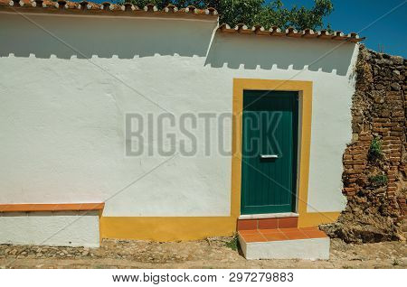 Closed Door In A Plaster White Wall Next To A Stone And Bricks Wall In Sunny Day, From A Street Of E