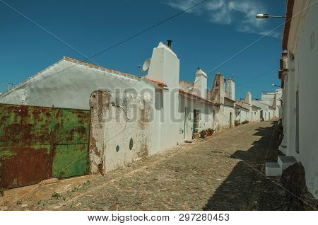 Humble White Wall Houses With Iron Garage Gate In A Sunny Day, On The Cobblestone Main Street Of Evo