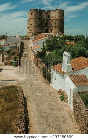 People Walking Up The Main Cobblestone Street In A Sunny Day Towards The Castle Of Evoramonte. A Tin