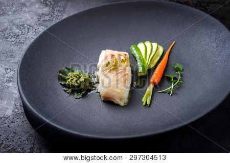 Fried Danish skrei cod fish filet with vegetable, lettuce and coriander pesto as top view on a modern design plate 