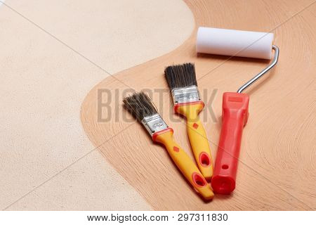 Yellow paint brushes and red roller lying on textural double background consisting of two beige shades. Top view with copy space, Concept of construction or design office