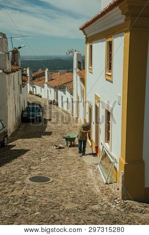 Evoramonte, Portugal - July 6, 2018. Man sweeping the front of colorful house at the main street of Evoramonte. A tiny fortified civil parish over hill where stands out its historic castle in Portugal