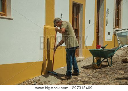 Evoramonte, Portugal - July 6, 2018. Mason working in front of colorful house at the main street of Evoramonte. A tiny fortified civil parish over hill where stands out its historic castle in Portugal