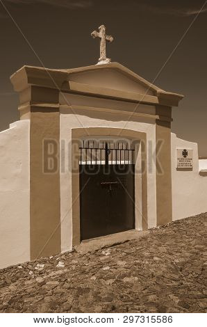 Evoramonte, Portugal - July 6, 2018. Colorful gateway in graveyard wall in Evoramonte. A tiny fortified civil parish over hill where stands out its historic castle in Portugal. Black and white photo.