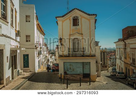 Elvas, Portugal - July 07, 2018. Street with colorful old houses in a narrow causeway and elders walking at Elvas. A gracious star-shaped fortress city on the easternmost frontier of Portugal.