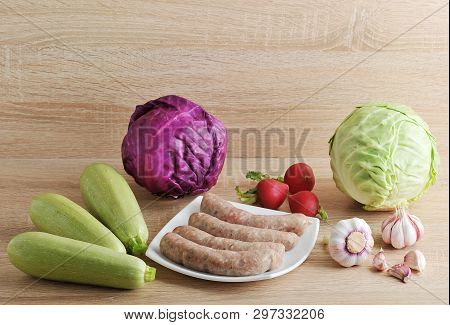 Raw Meat Sausages Kupaty And Vegetables - Cabbage, Zucchini, Radish And Garlic On Wooden Background