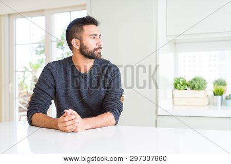 Handsome hispanic man wearing casual sweater at home looking to side, relax profile pose with natural face with confident smile.