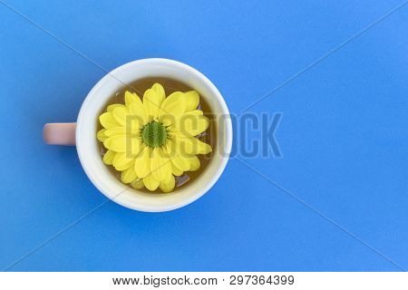 Yellow Chrysanthemum Flower Floating In A Tea Cup, Blue Background With Copy Space