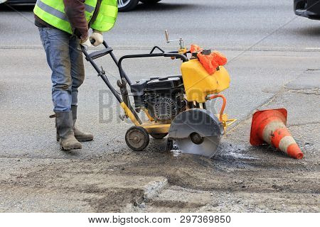 Worker Cuts A Piece Of Bad Asphalt With A Gasoline Cutter During Road Construction.