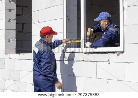 Workers Install Glazing In A House Under Construction, Make Measurements, Drill, Saw Grinder