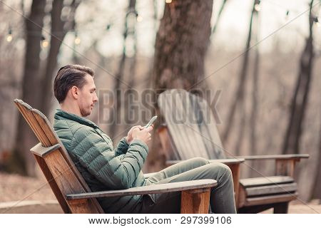 Caucasian Tourist Boy With Cellphone Outdoors In Cafe. Man Using Mobile Smartphone.
