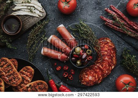 Different Types Of Spanish Appetizers. Jamon, Chorizo, Fuet And Anchovy Fillets On Dark Background T