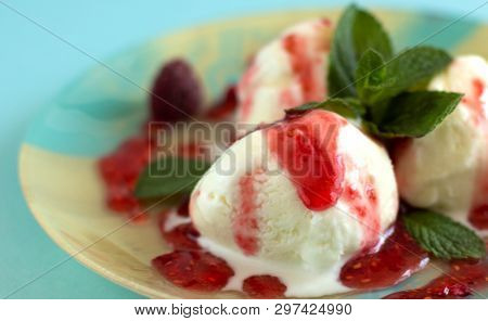 Close-up Of Three Vanilla Ice Cream Balls With Raspberry Jam And Mint On A Blue-beige Plate With A B