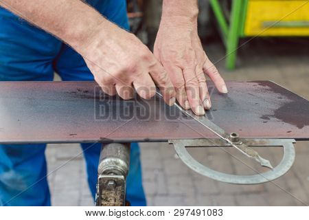 Metalworker with angle meter measuring strip of metal for later cutting