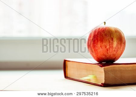 Red Book Near The Window With A Red Apple On Top. Knoweldge Apple.