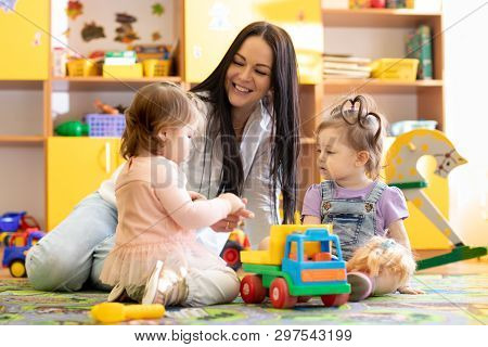 Children Kids Toddlers Playing With Teacher In Kindergarten. Nursery Babies Sitting On Floor Togethe