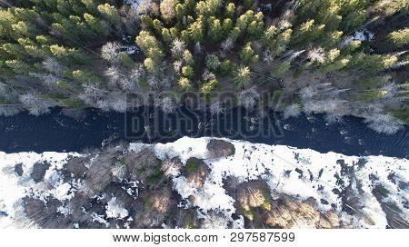 Aerial View Of A River In The Forest With Snow Along The Banks.
