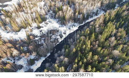 Aerial View Of A River In The Forest With Snow Along The Banks.