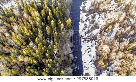 Aerial View Of A River In The Forest With Snow Along The Banks.