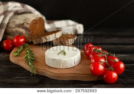 Camembert Cheese  With Rye Bread, Nuts, Cherry Tomatoes And Rosemary On A Wooden Board