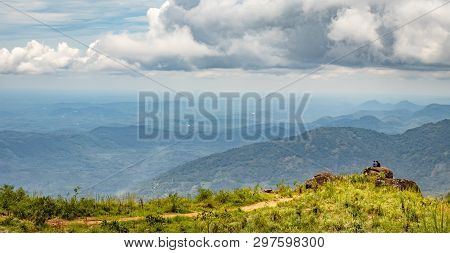 Two Person Sitting On The Rock For Wide Landscape View With Hill, Blue Sky And White Clouds.