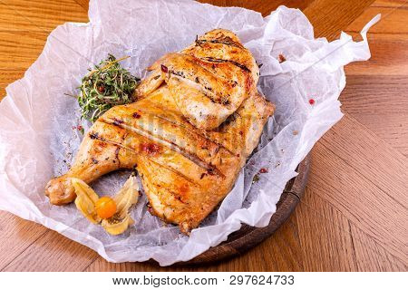 Grilled Chicken Tabaka Served With Herbs On Wooden Table