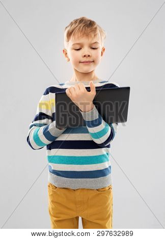 childhood and people concept - nice little boy in striped pullover with tablet pc computer over grey background