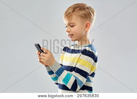 technology, childhood and people concept - little boy in striped pullover using smartphone over grey background