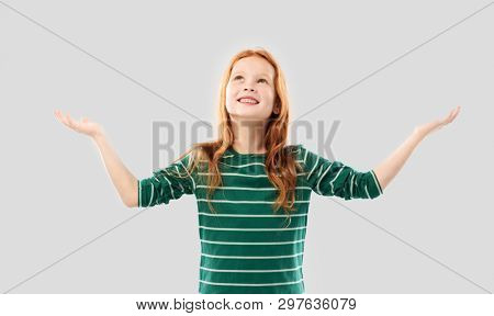 childhood, faith and thanks concept - grateful smiling red haired girl in green striped shirt looking up above over grey background