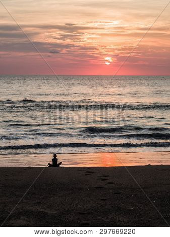 Silhouette Of An Indefinite Person In Lotus Position On A Sea Sandy Beach During A Beautiful Sunset.