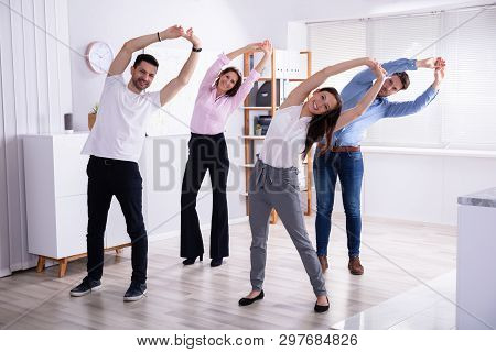 Group Of Happy Young Businesspeople Doing Stretching Exercise In Office