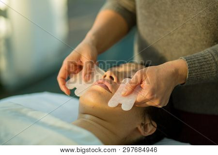 Young Woman Receiving Facial Rejuvenation Gua Sha Treatment With Rose Quartz In Acupuncture Wellness