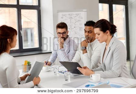 new job, hiring and employment concept - international team of recruiters looking at clipboard and having interview with asian female employee at office
