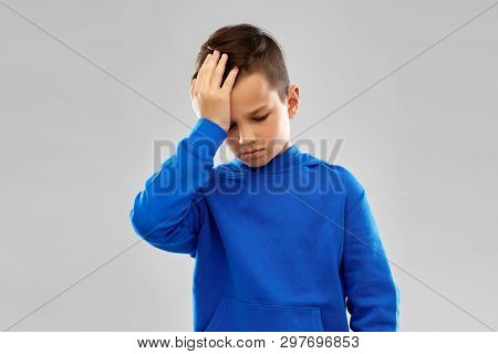 childhood, expressions and people concept - sick boy in slue hoodie suffering from headache over grey background