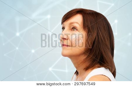 beauty, cosmetology and anti-age technology concept - portrait of senior woman with low poly grid on her cheek over blue background