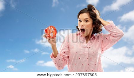 time, emotions and bedtime concept - shocked young woman in pajama with alarm clock showing half past six over blue sky and clouds background