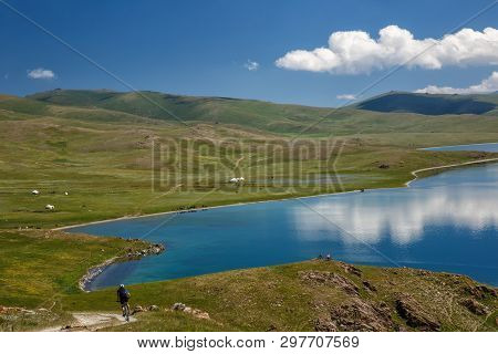 Guy Downhill On A Bike To A Magnificent Mountain Lake. The Sky With Beautiful Clouds Reflected On Th