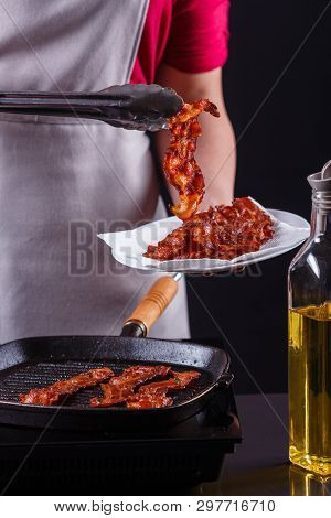 Young Woman In A Gray Apron Fries Bacon