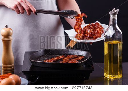 Young Woman In A Gray Apron Fries Bacon
